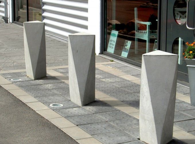 Trzy słupki wykonane z betonu umieszczone na kostce brukowej.