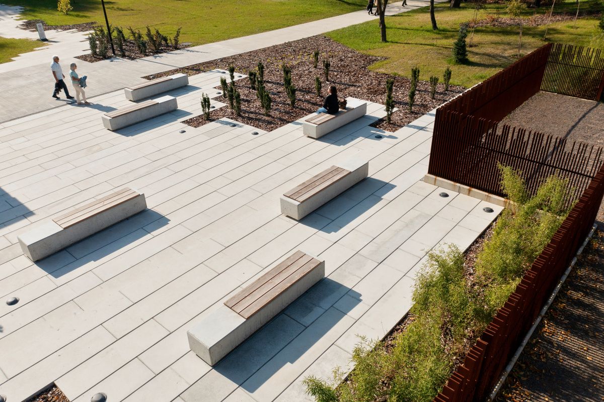 Płyty betonowe wykorzystane w parku. Na betonowych płytach umieszczone są betonowe ławki z drewnianym siedziskiem.