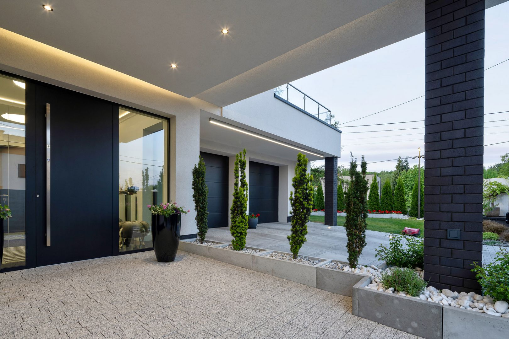 Betonowe murki oporowe z drzewkami. Widok na bramę garażową