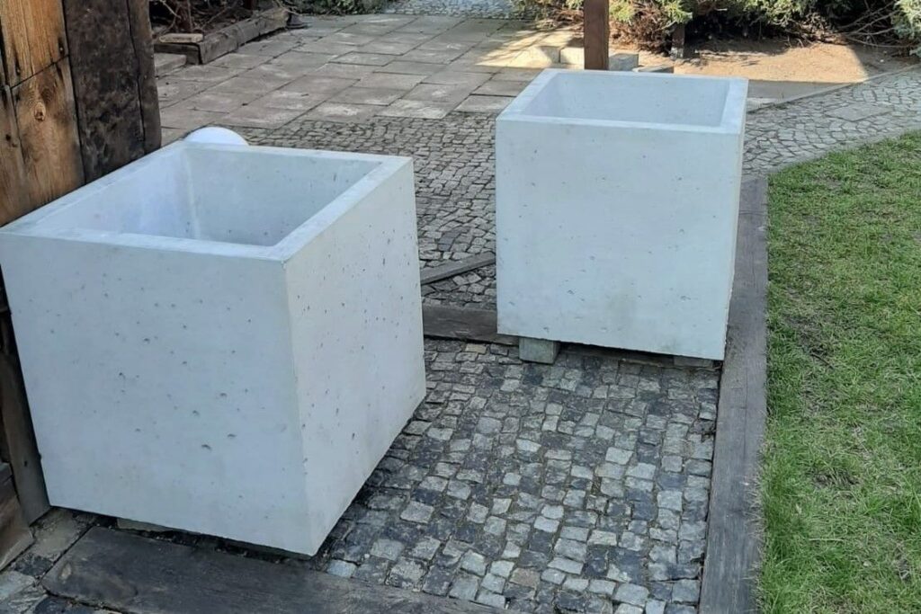Dwie duże, puste betonowe donice na kostce brukowej