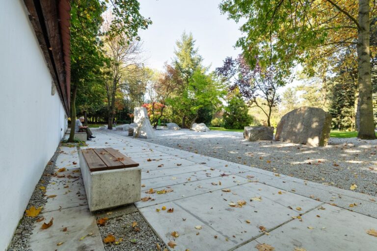 Park z leżącymi jesiennymi liśćmi na betonowych płytach z kamieniami i drzewami w tle