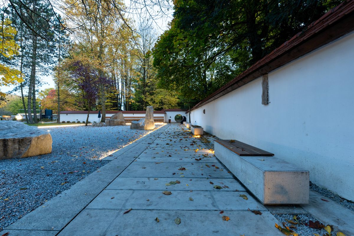 Podświetlane betonowe ławki z drewnianym siedziskiem obok białego muru.